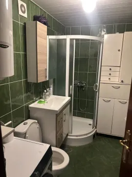 Kupatilo sa tuš kabinom, umivaonikom, WC šoljom i zelenim pločicama na zidovima. - image 4
