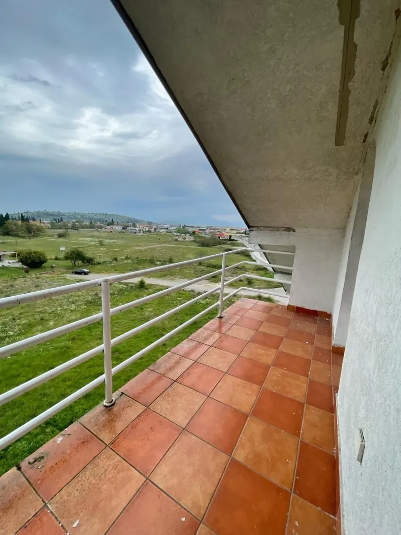 Prostrani balkon popločan pločicama sa pogledom na zeleni pejzaž.