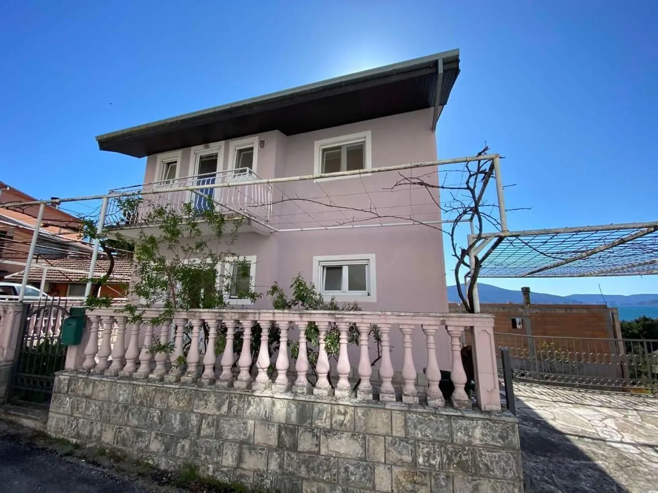 Pogled na dvospratnu kuću sa ograđenim dvorištem i terasom.