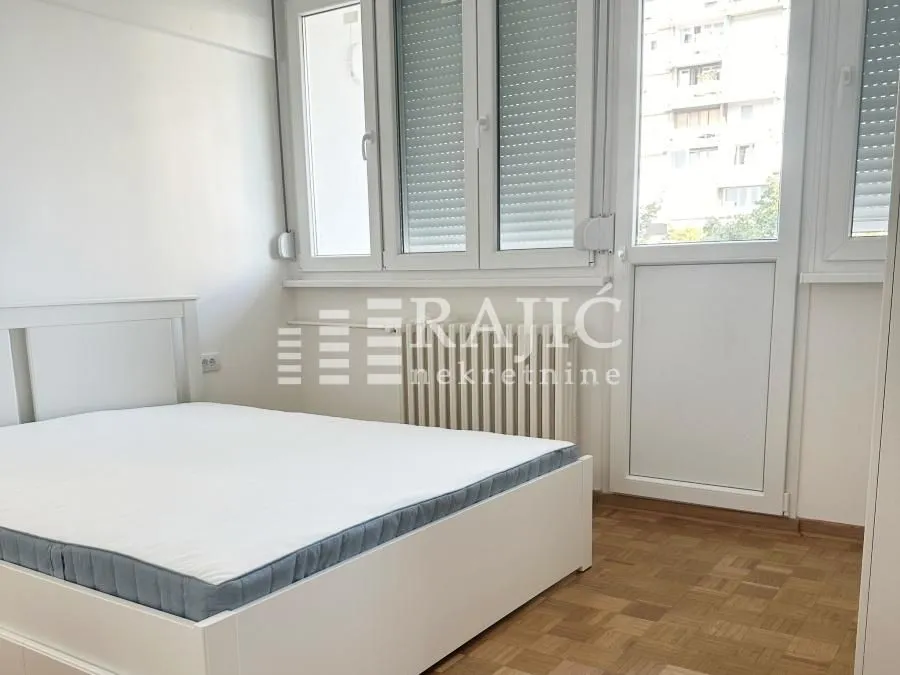 Bright bedroom with a white bed and parquet flooring.