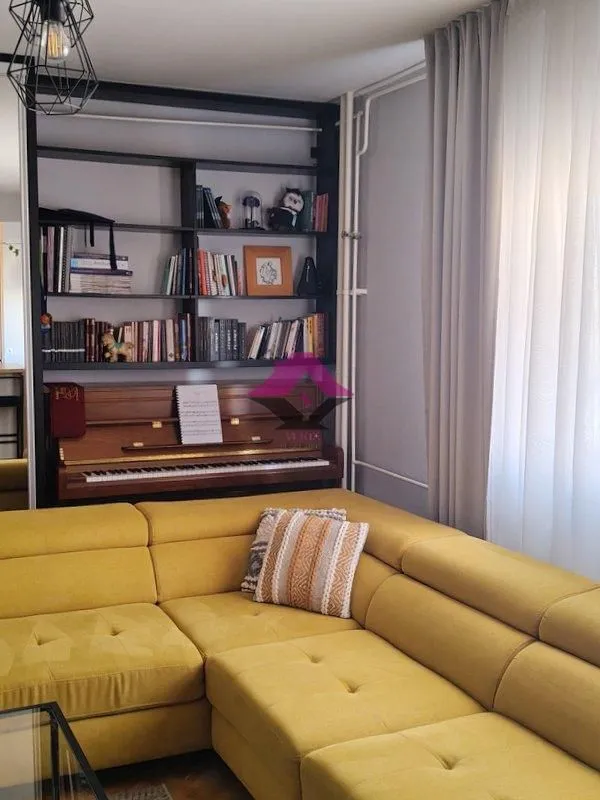 Living room with a yellow sectional sofa, piano and a bookshelf.