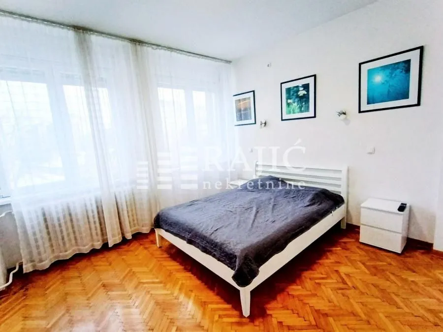 Bright bedroom with a double bed, white furniture and parquet flooring.