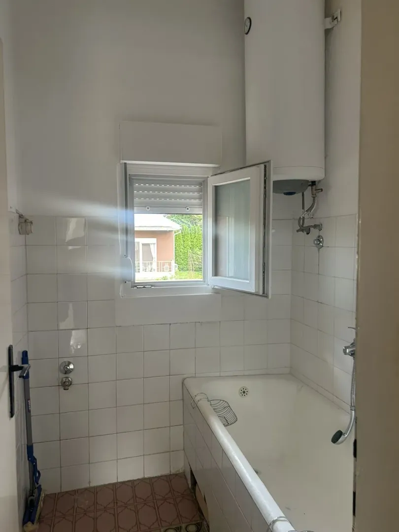 A simple bathroom featuring a bathtub, window, and water heater.