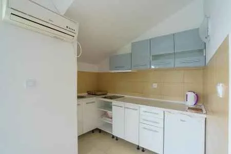 Manja kuhinja sa bijelim elementima i klima uređajem na zidu.