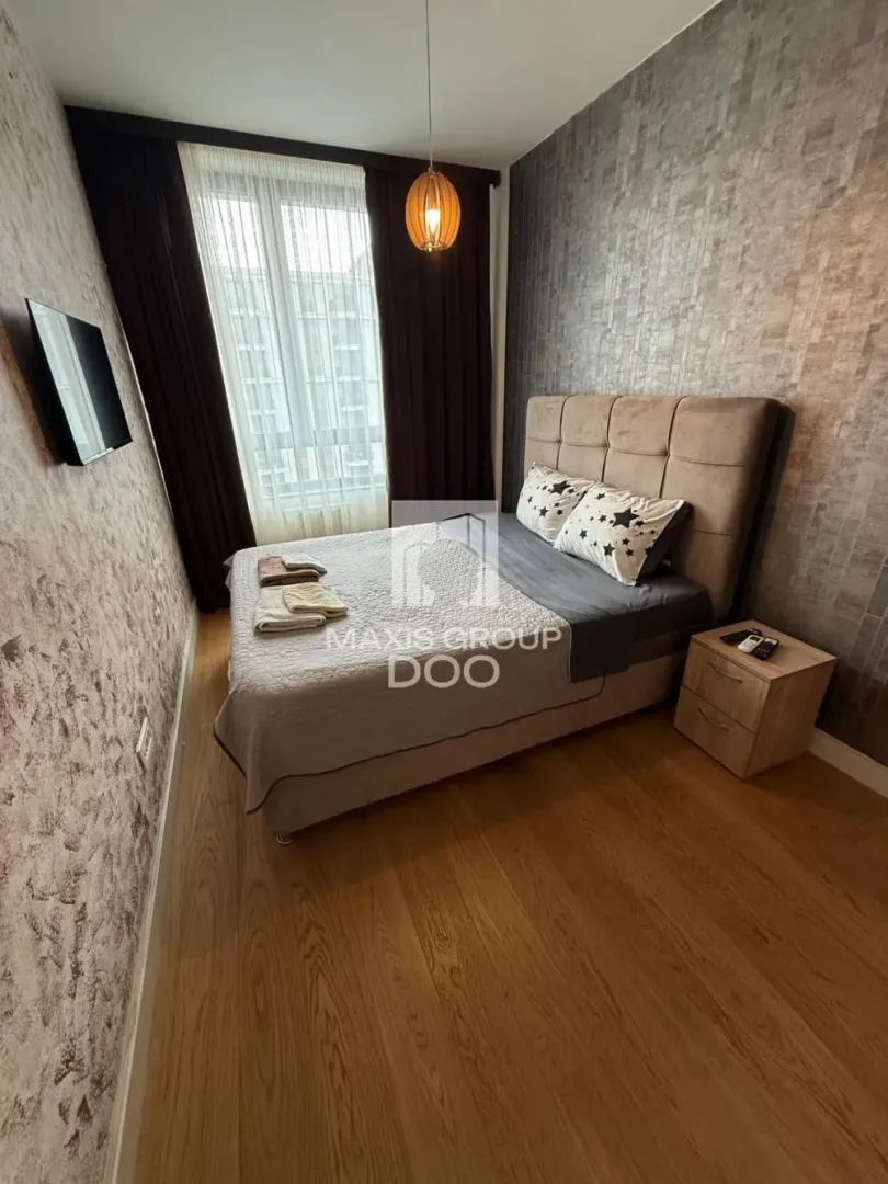 Nameštena spavaća soba sa bračnim krevetom, noćnim stočićem i TV-om.