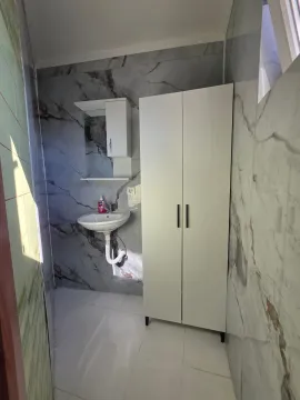 Bathroom with a sink, mirror, and white cabinet against marble-effect tiles. - image 19