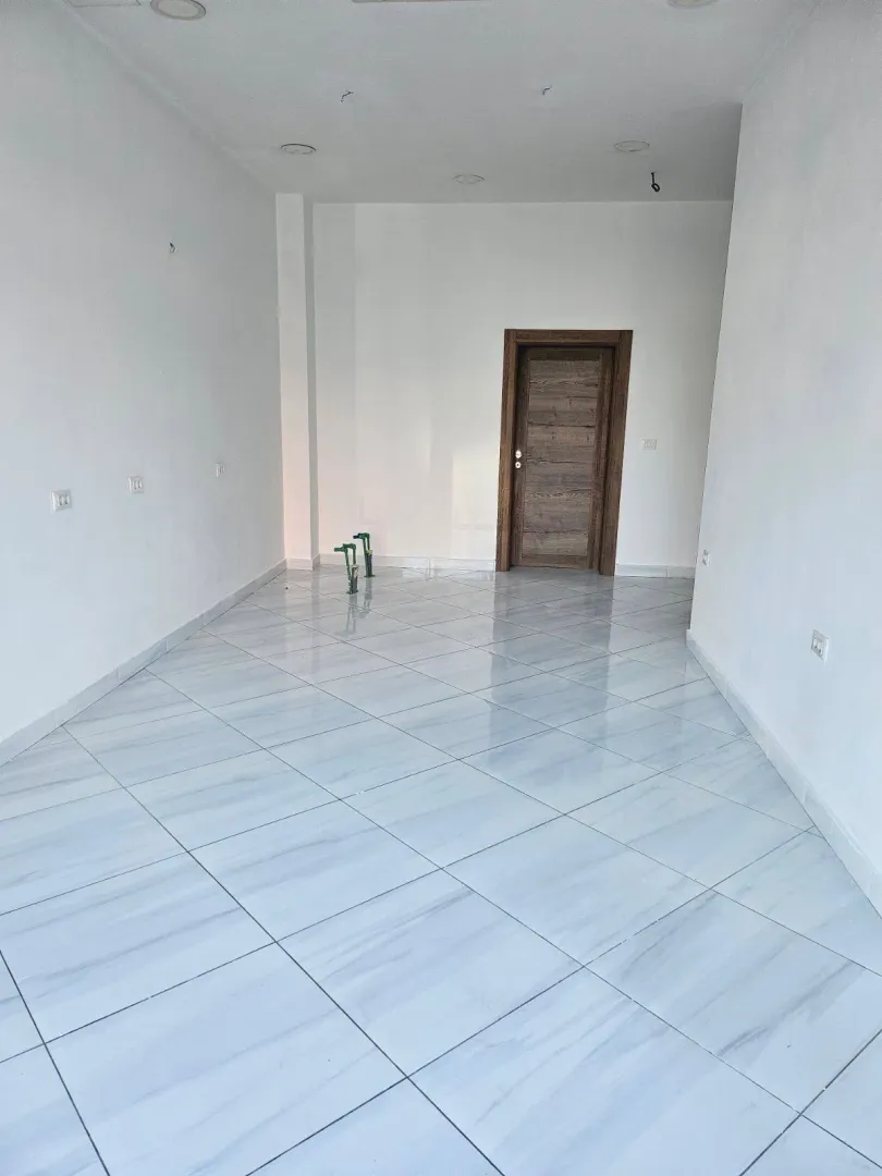 Empty room with white walls, tiled flooring, and a wooden door.