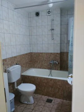 Smaller bathroom with a bathtub, toilet, and brown-toned tiles. - image 4