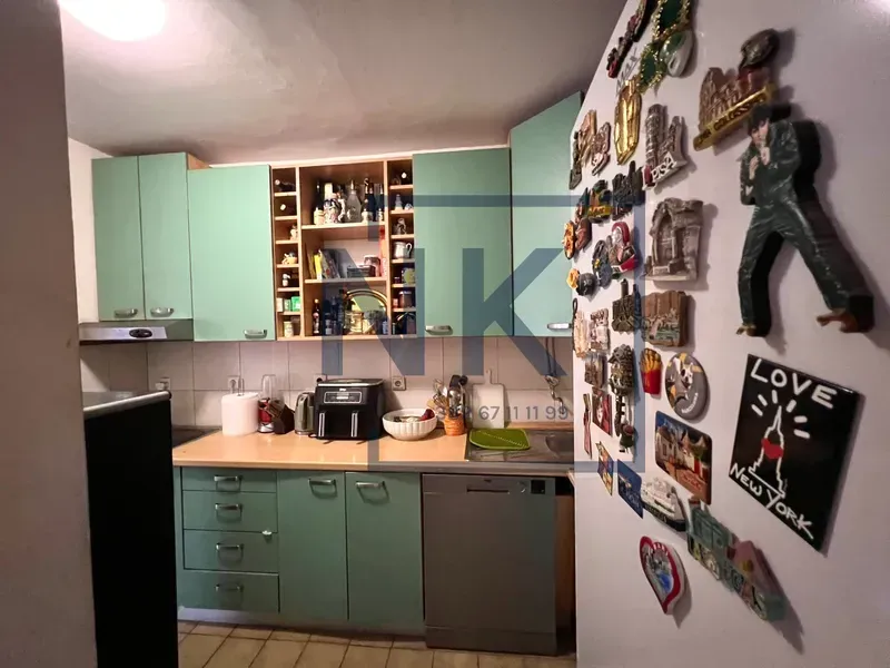 Kuhinja sa zelenim elementima i zidom ukrašenim suvenirima.