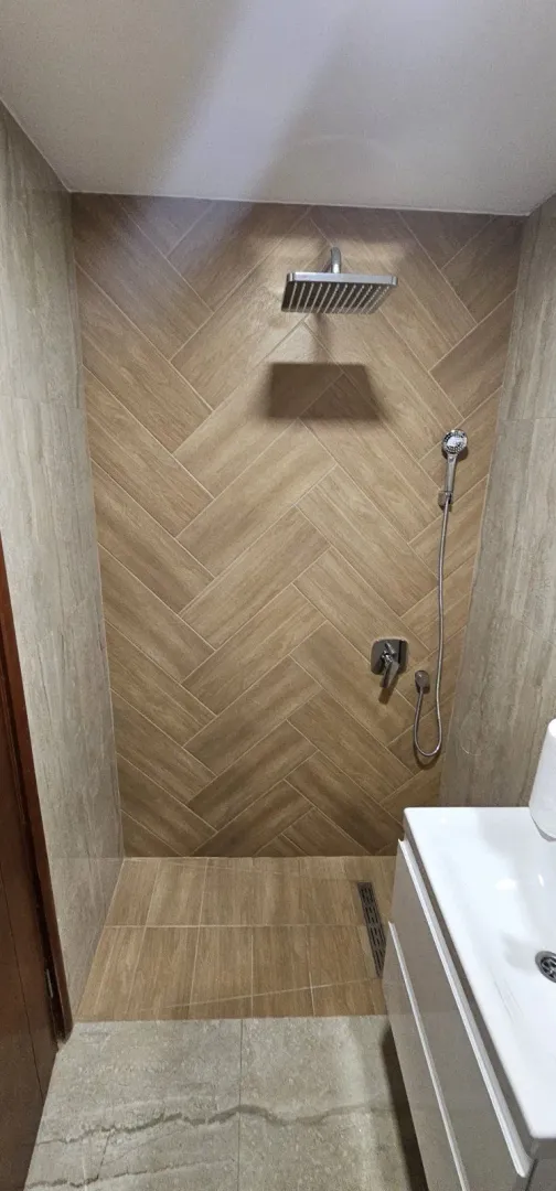 Moderno kupatilo sa tuš kabinom obloženom pločicama u dezenu drveta.