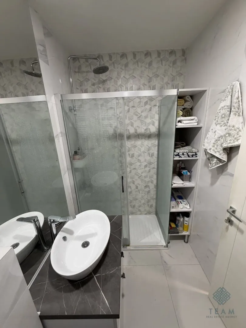 Moderne kupatilo sa umivaonikom, tuš kabinom i ugradnim policama.
