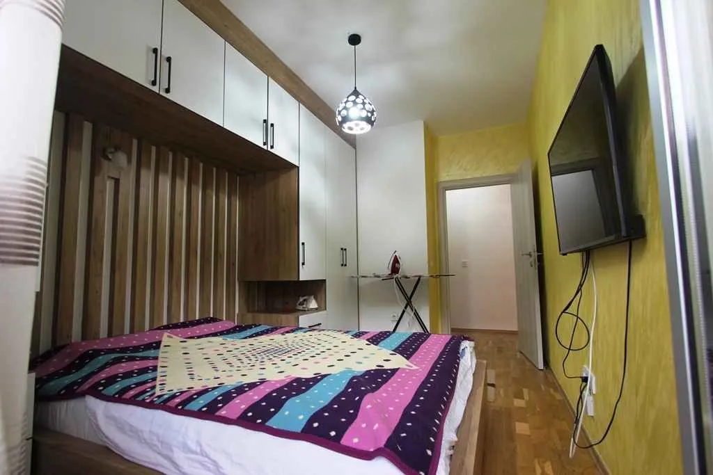 Namještena spavaća soba sa bračnim krevetom, ugradnim plakarima i televizorom na zidu.