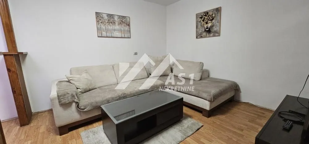 Dnevna soba sa ugaonom garniturom, stočićem i slikama na zidu.