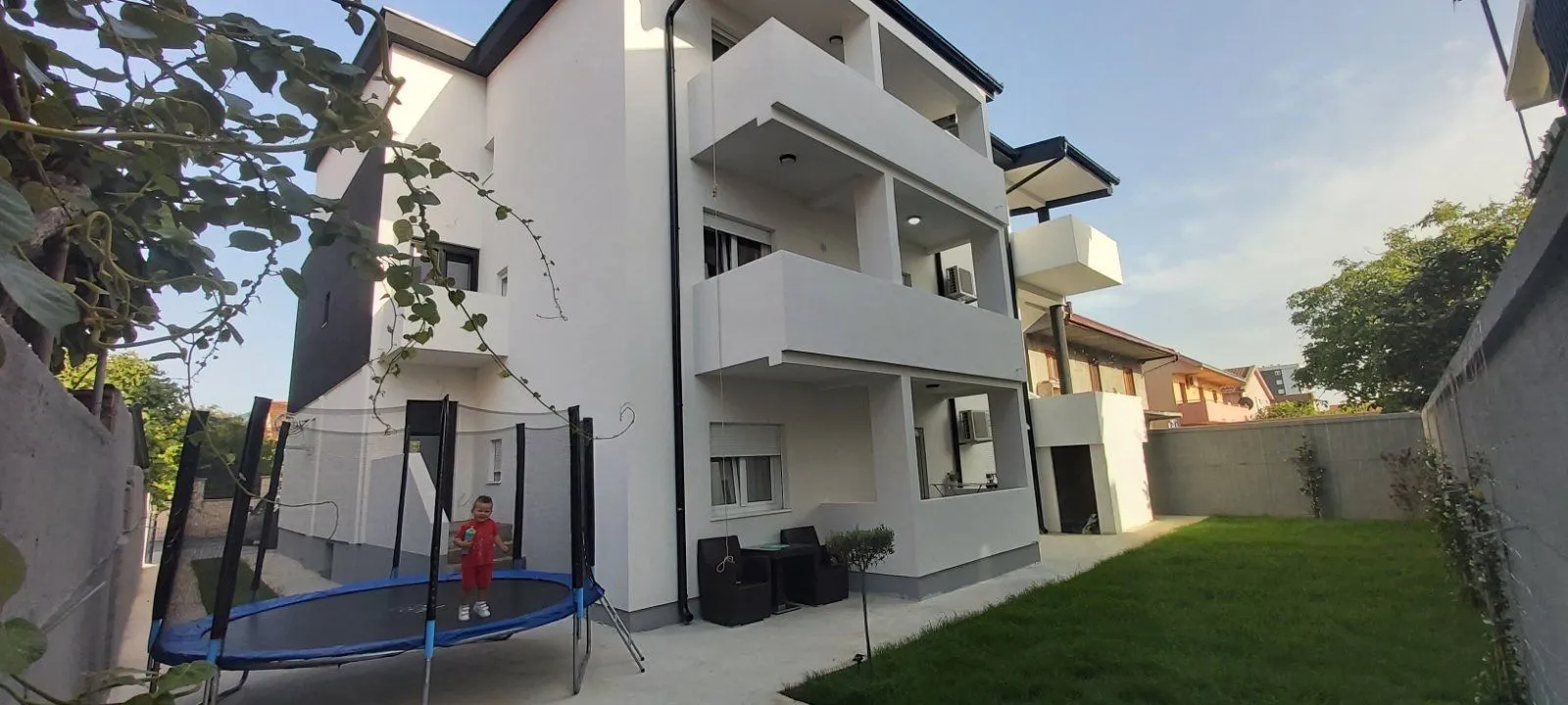 Exterior of a modern building with a yard and a trampoline.