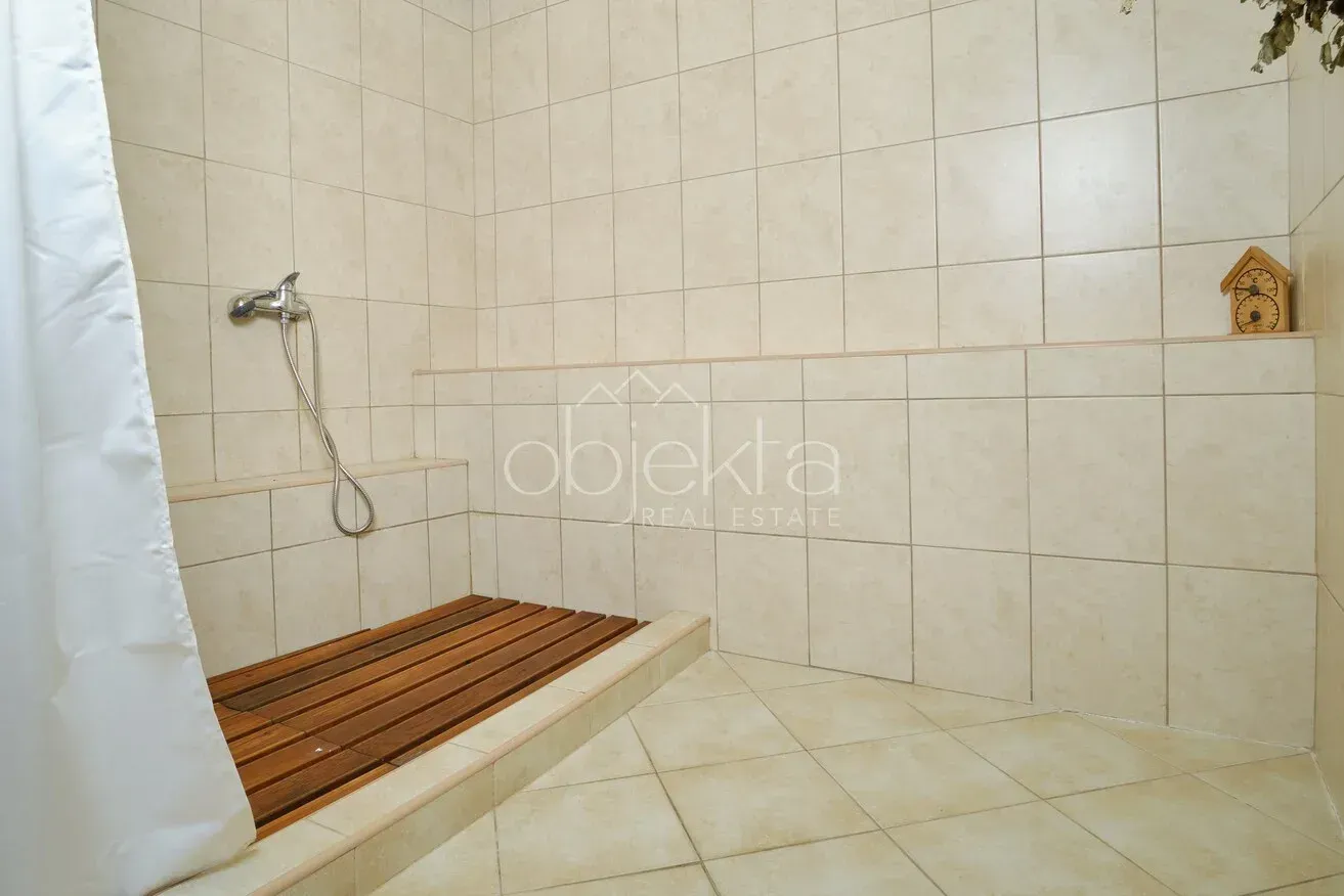 Shower cabin with ceramic tiles and a wooden grid on the floor.