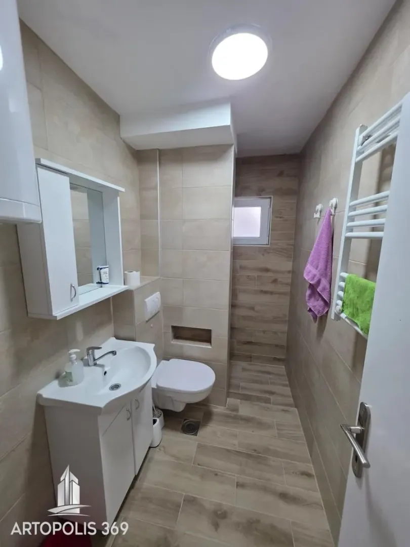 Small tiled bathroom equipped with a vanity sink, toilet, and shower area.