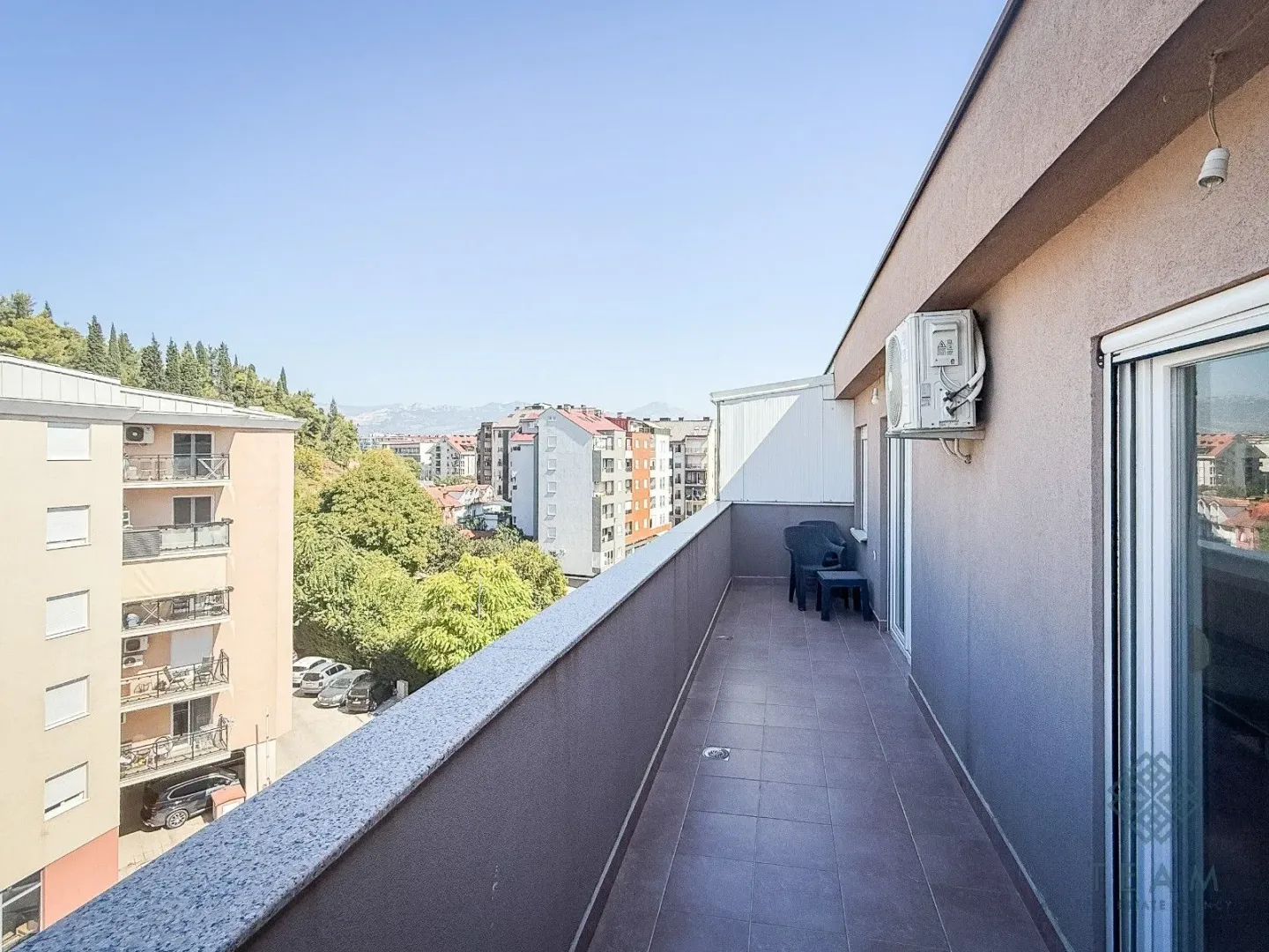 Prostrani popločani balkon sa pogledom na okolne zgrade i zelenilo.