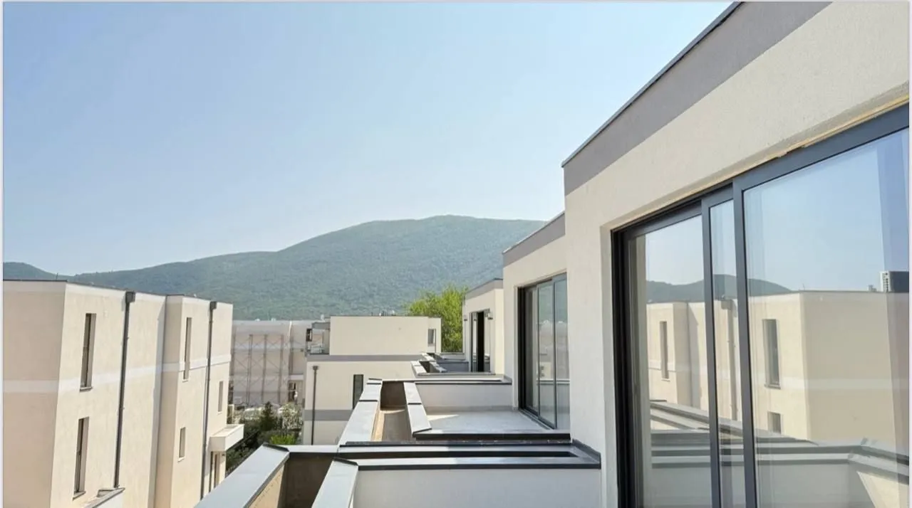 View from the terrace towards neighboring buildings and a hill in the background.