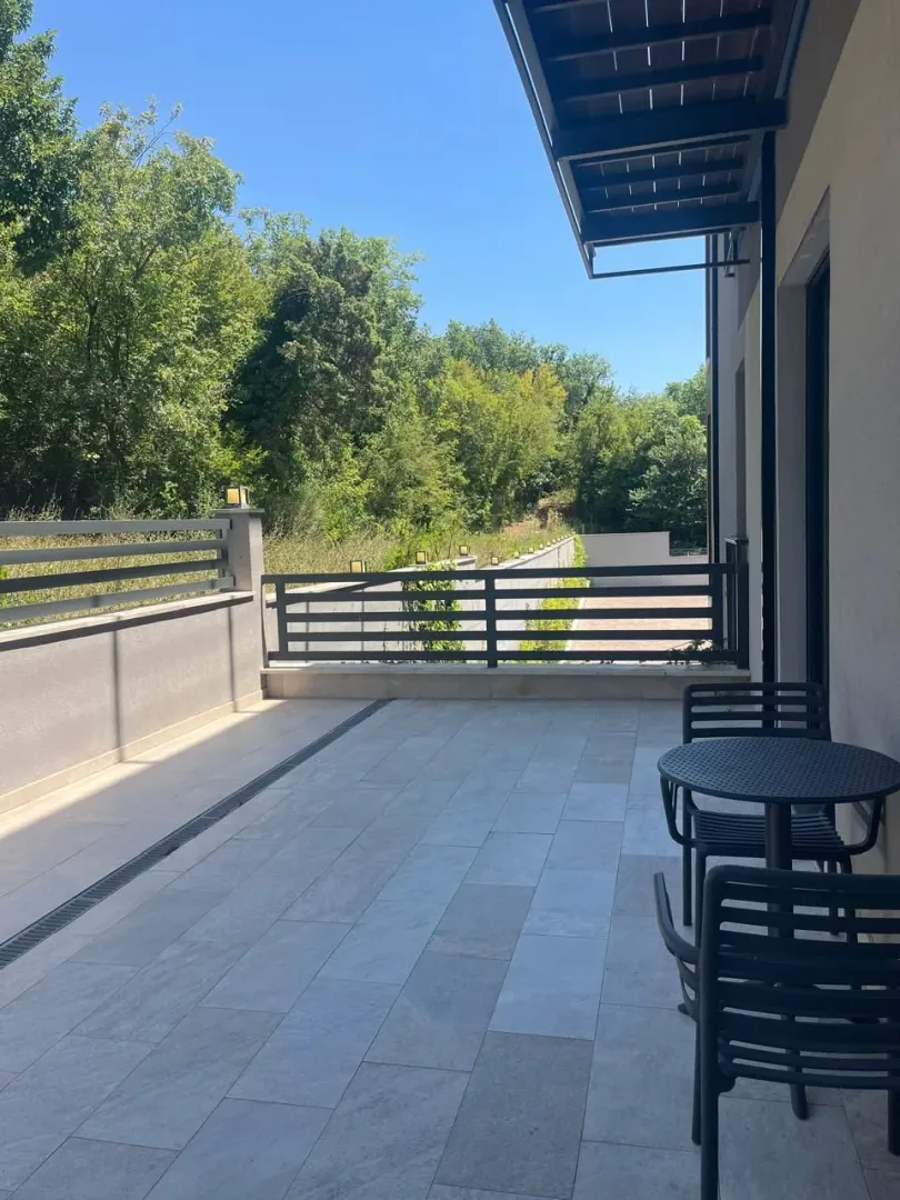 Prostrana terasa sa garniturom za sjedenje i pogledom na zelenilo.