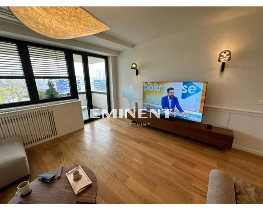 Dnevna soba sa drvenim podom, televizorom i izlazom na terasu.