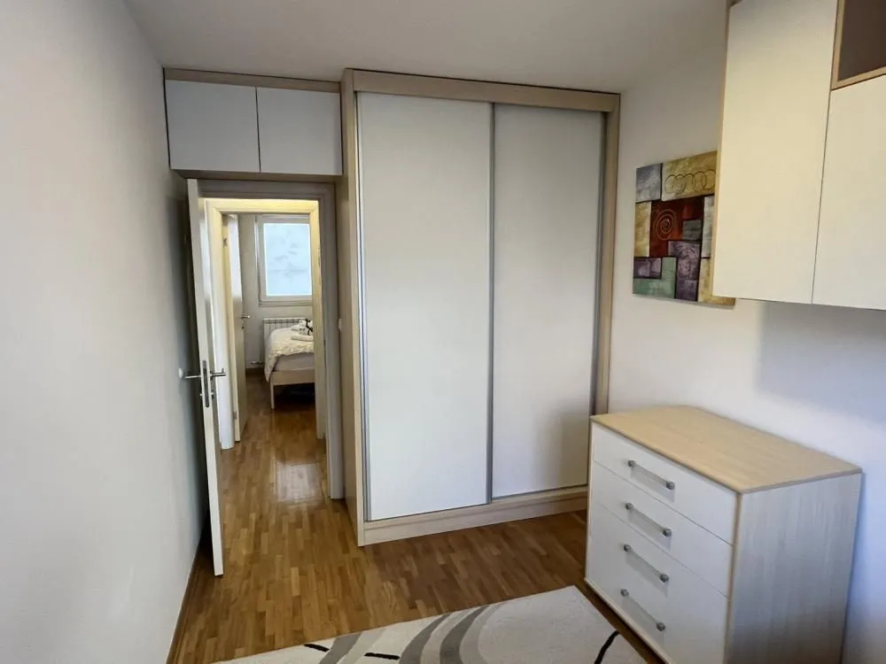 Spavaća soba sa ugradnim ormanom, komodom i laminatnim podom.