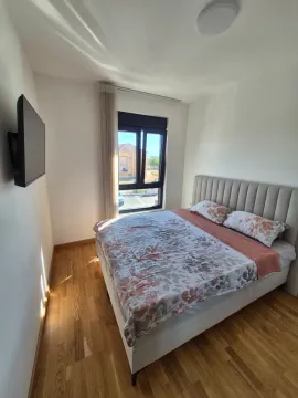 Spavaća soba sa bračnim krevetom, drvenim podom i zidnim televizorom. - image 3