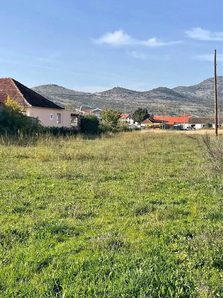Pogled na prostrano zemljište sa okolnim kućama i brdima u pozadini.