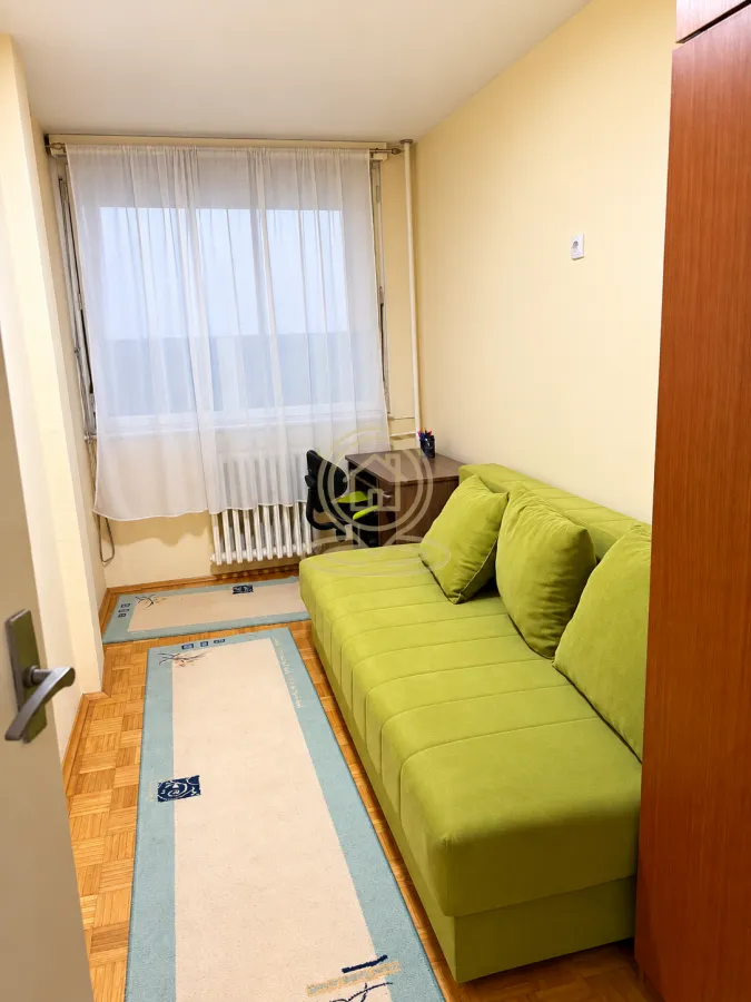 Manja spavaća soba sa zelenim kaučem i pisaćim stolom.