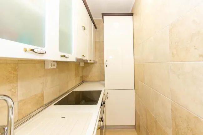 Small equipped kitchen with white cabinets and ceramic wall tiles.