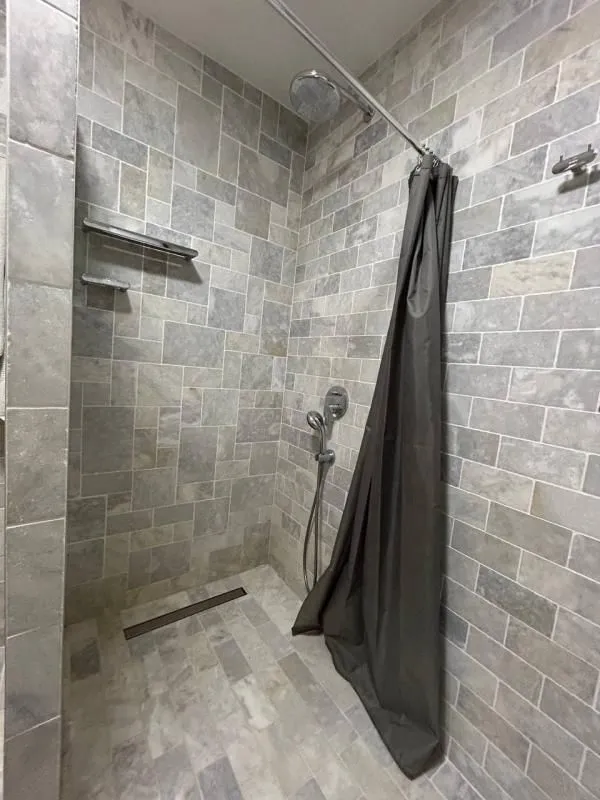 Tuš kabina obložena kamenim pločicama sa tuš zavjesom.