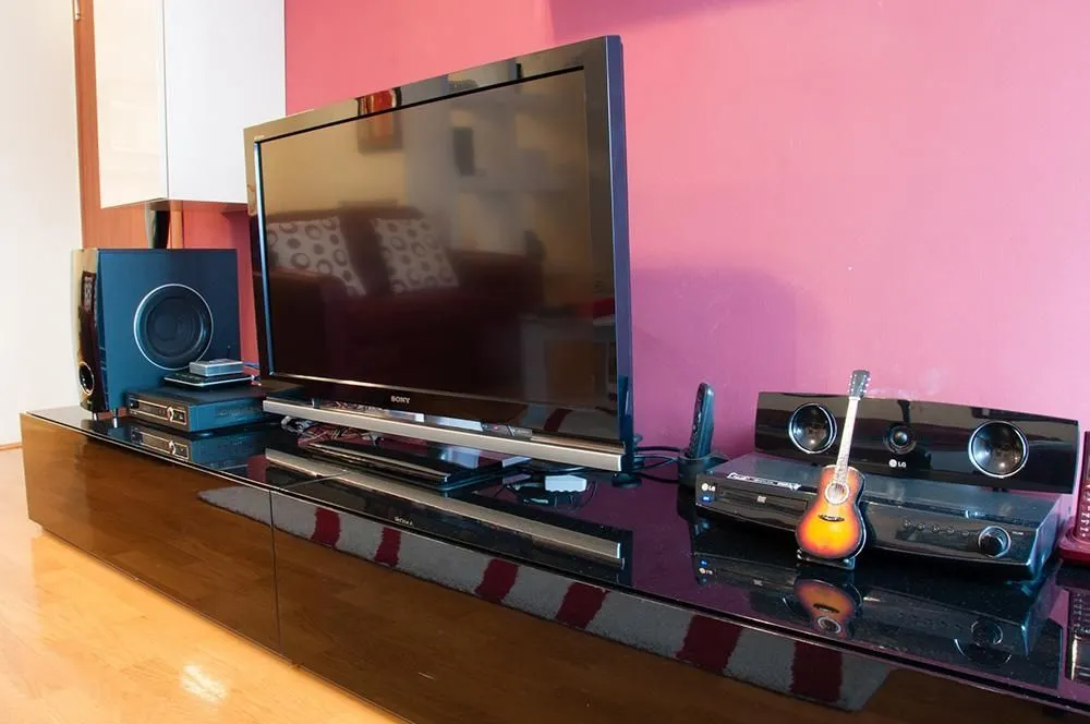 Living room with a television on a media console and a pink wall.