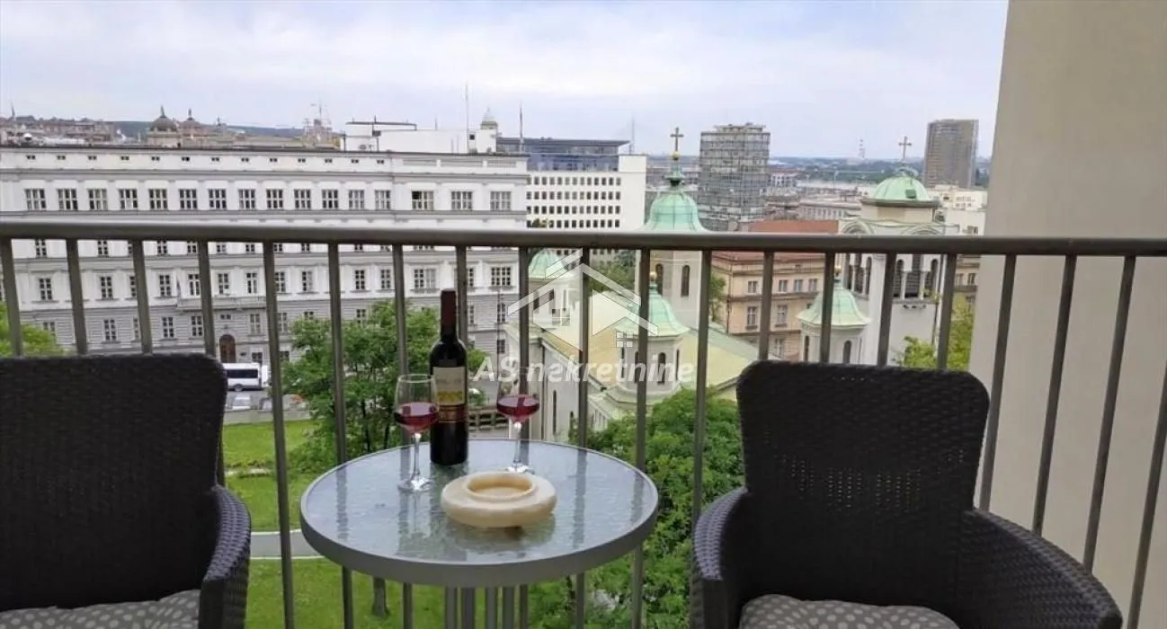 Furnished balcony with a table, chairs, a bottle of wine, and a city view.