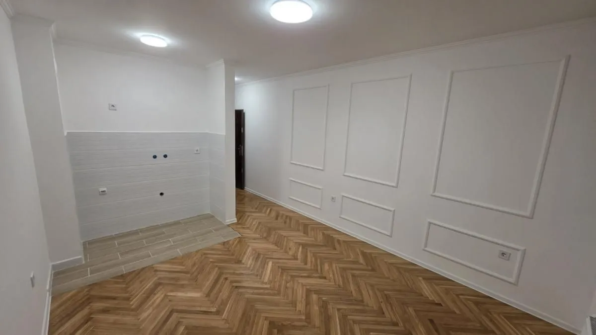 Nenameštena kuhinja sa pločicama i drvenim podom u novom stanu.