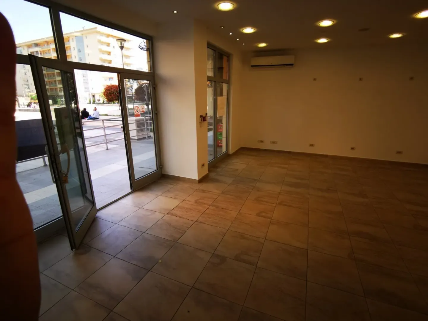 An empty commercial space with tiled flooring and large glass doors.