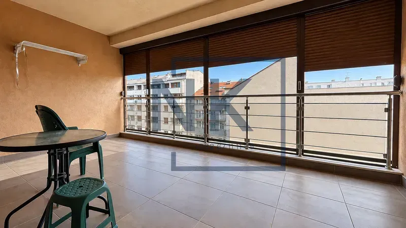 Zastakljena terasa sa stolom, stolicama i pogledom na grad.