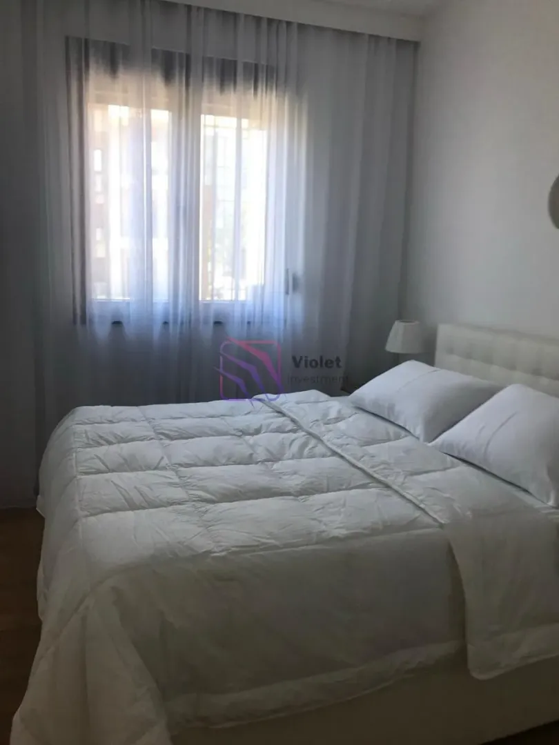 Spavaća soba sa bračnim krevetom i prozorom sa bijelim zavjesama.