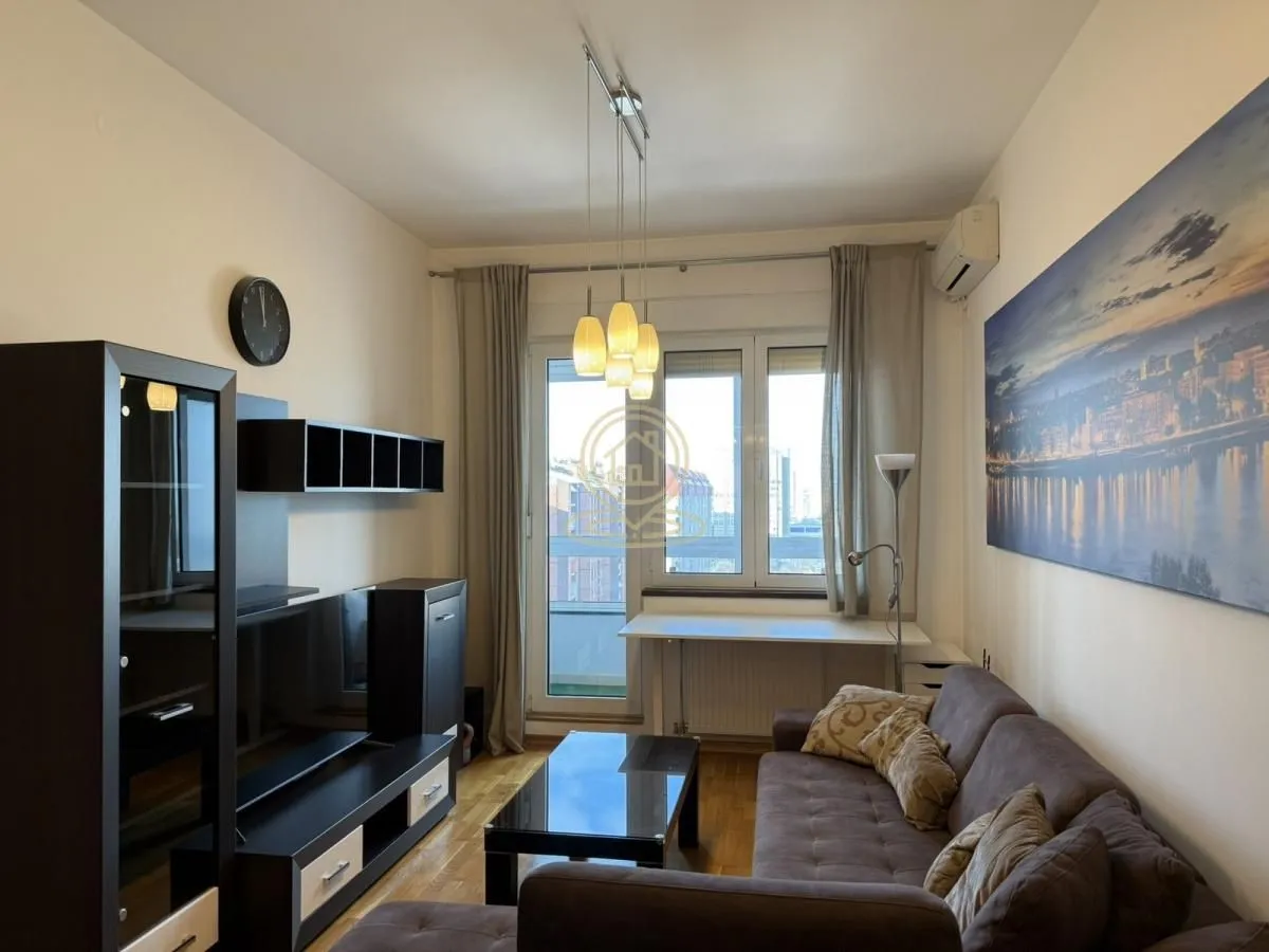 Namešten dnevni boravak sa garniturom, TV komodom i izlazom na balkon.