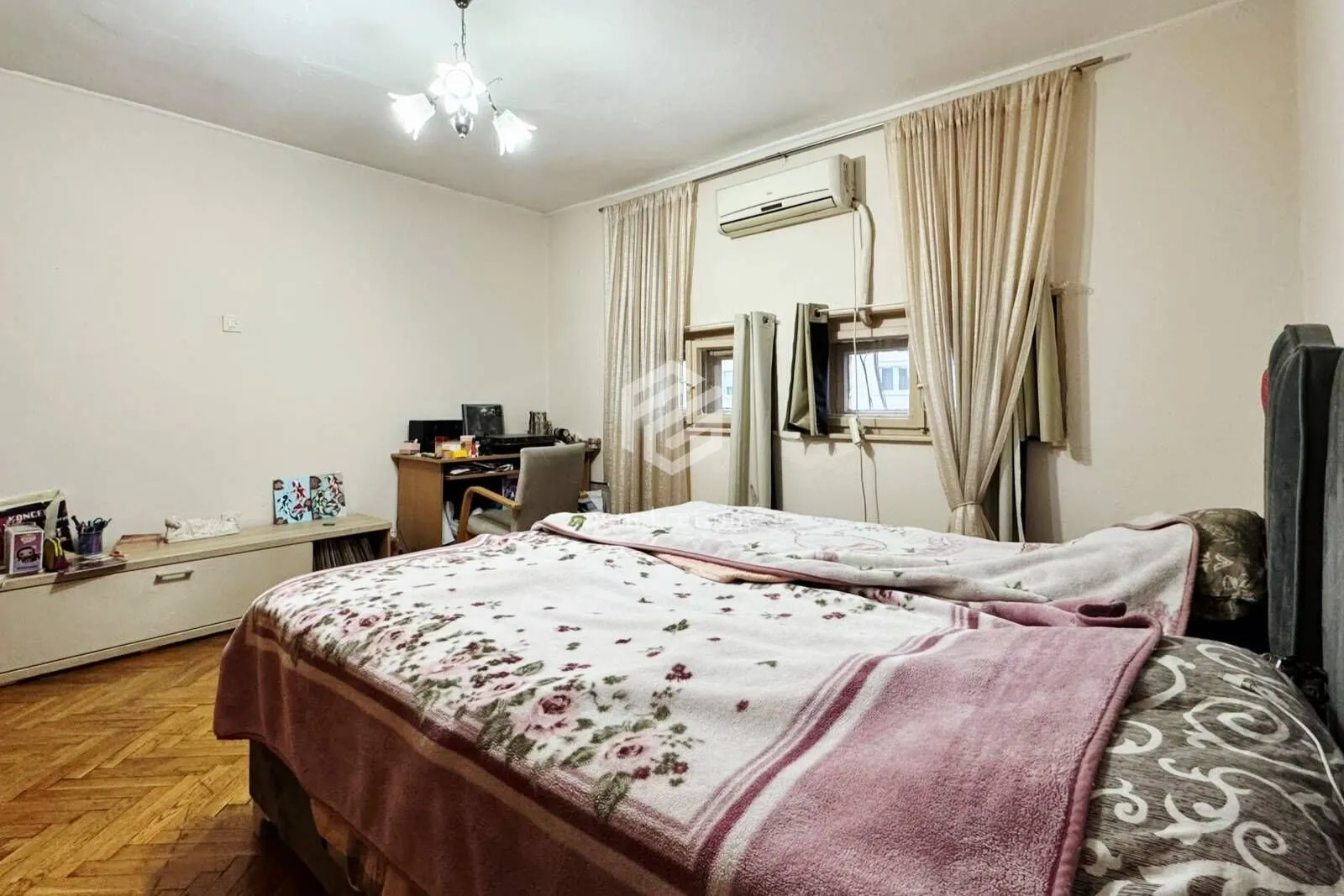 Namještena spavaća soba sa bračnim krevetom, radnim stolom i prozorima sa zavesama.