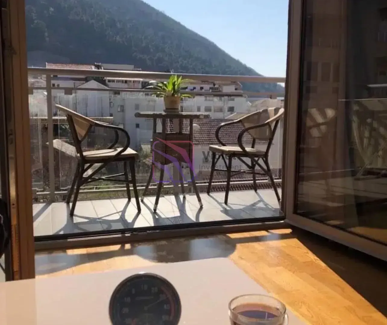 Manji namješten balkon sa stolom i dvije stolice s pogledom na naselje.