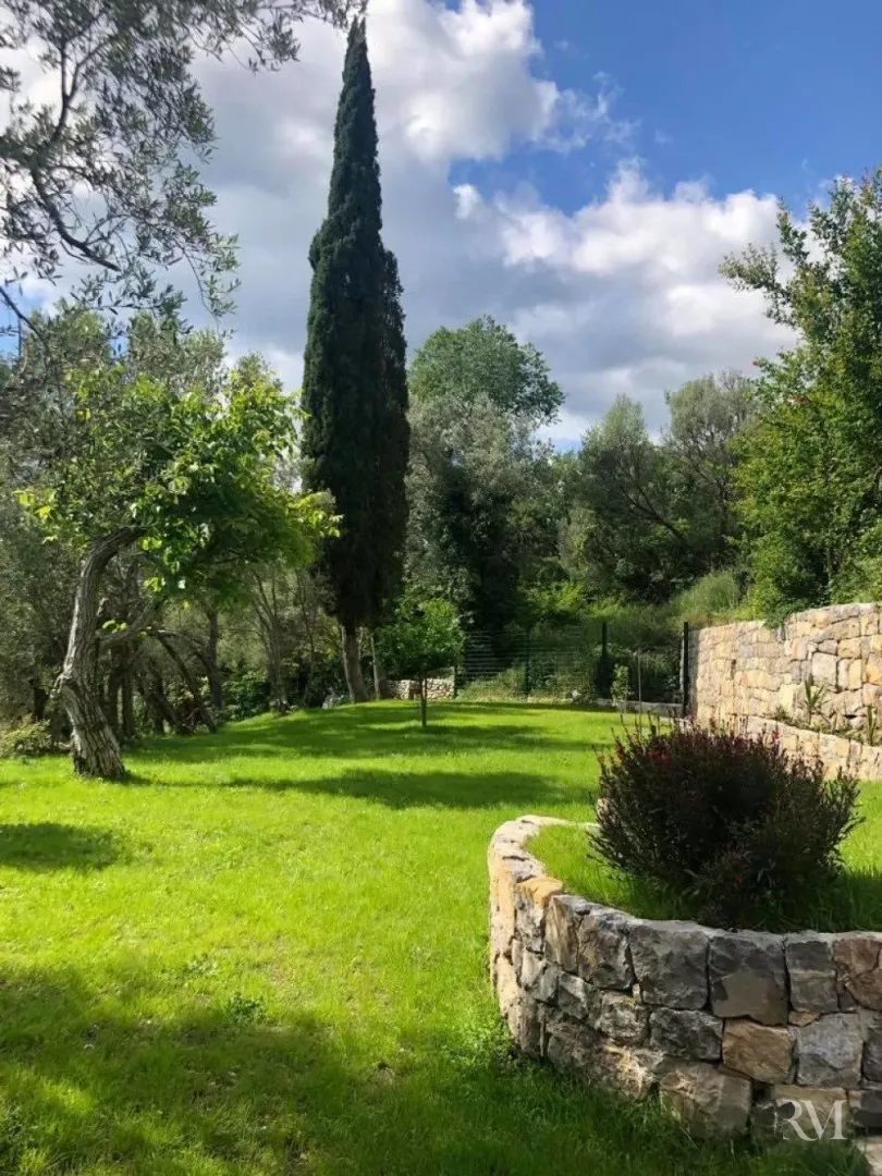 Landscaped yard with lawn, trees, and a stone wall.