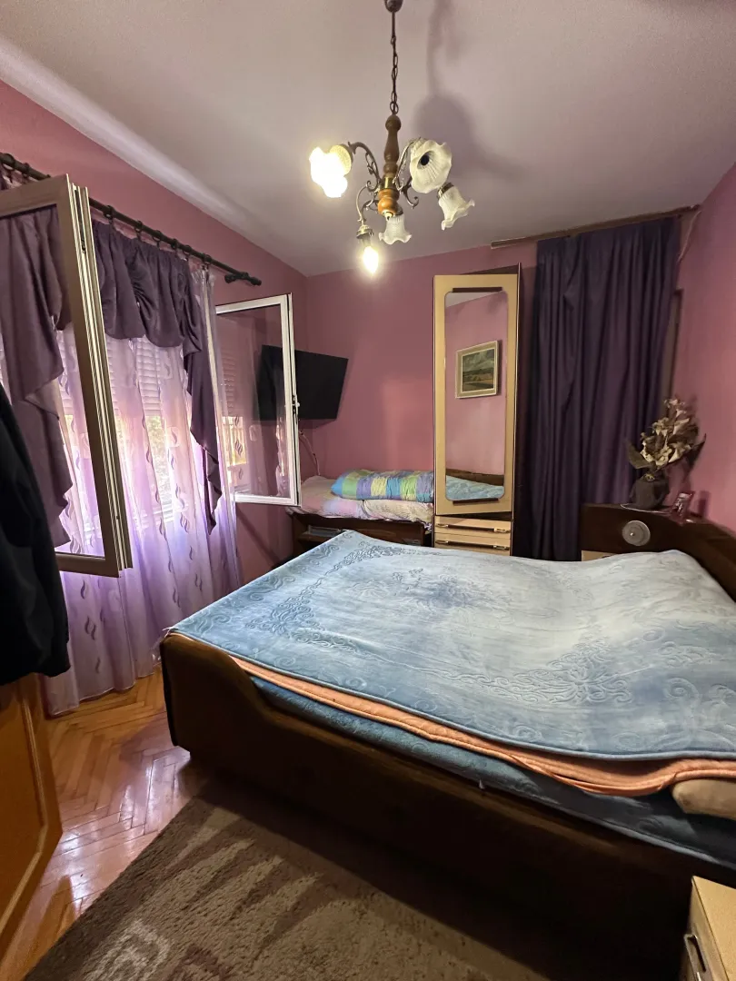 Spavaća soba sa bračnim krevetom, ljubičastim zidovima i lusterom.