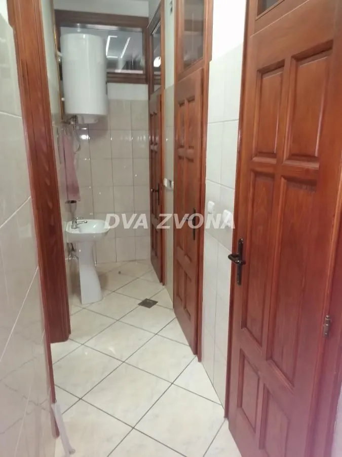 Small bathroom with tiled walls, washbasin, water heater, and wooden doors.