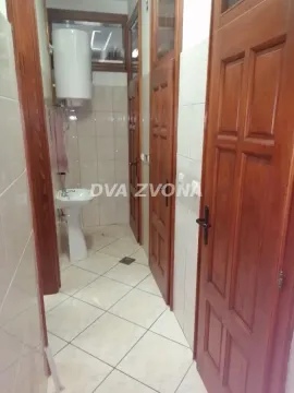 Small bathroom with tiled walls, washbasin, water heater, and wooden doors. - image 11