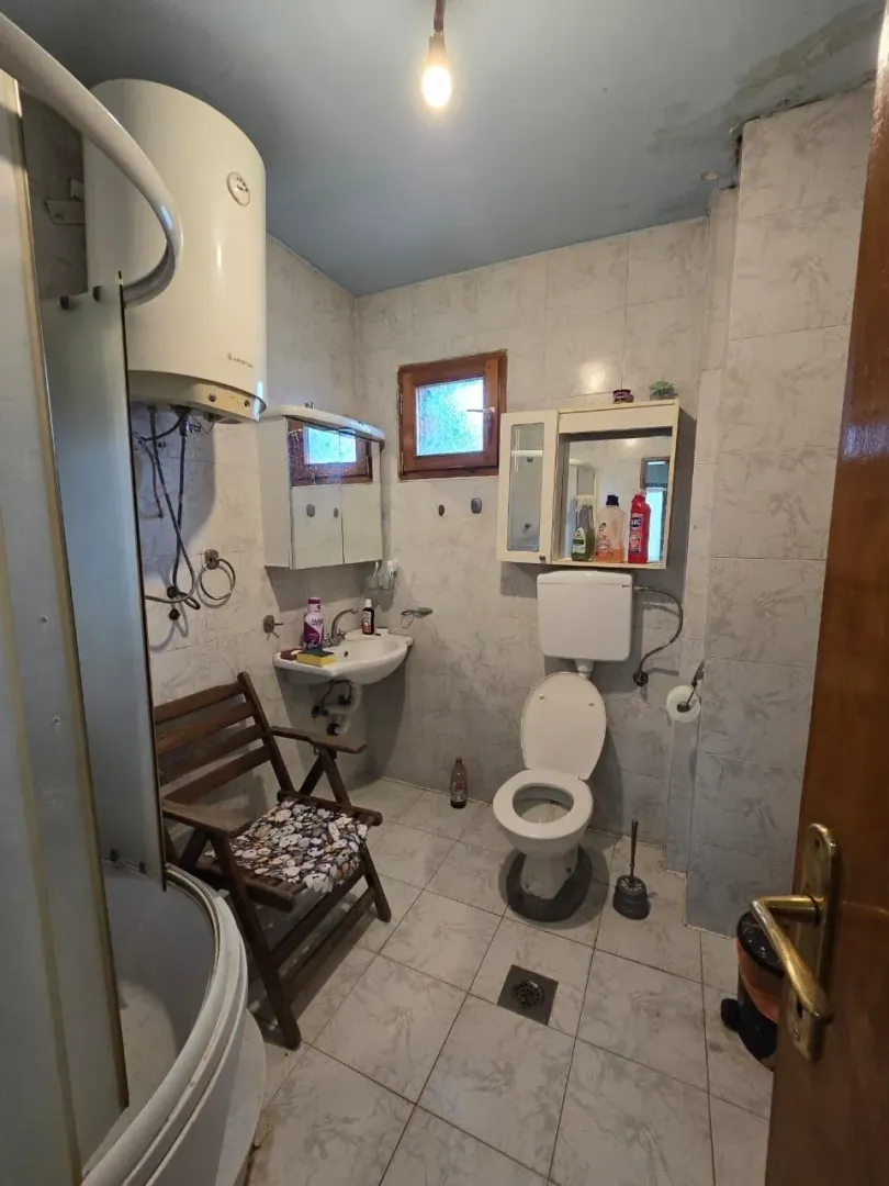 Jednostavno kupatilo sa tuš kabinom, bojlerom i wc šoljom.