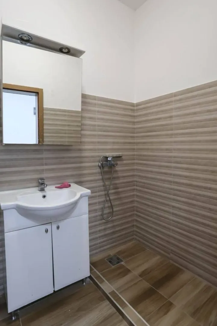 Small bathroom with a sink, mirror, and a shower area with brown-toned tiles.