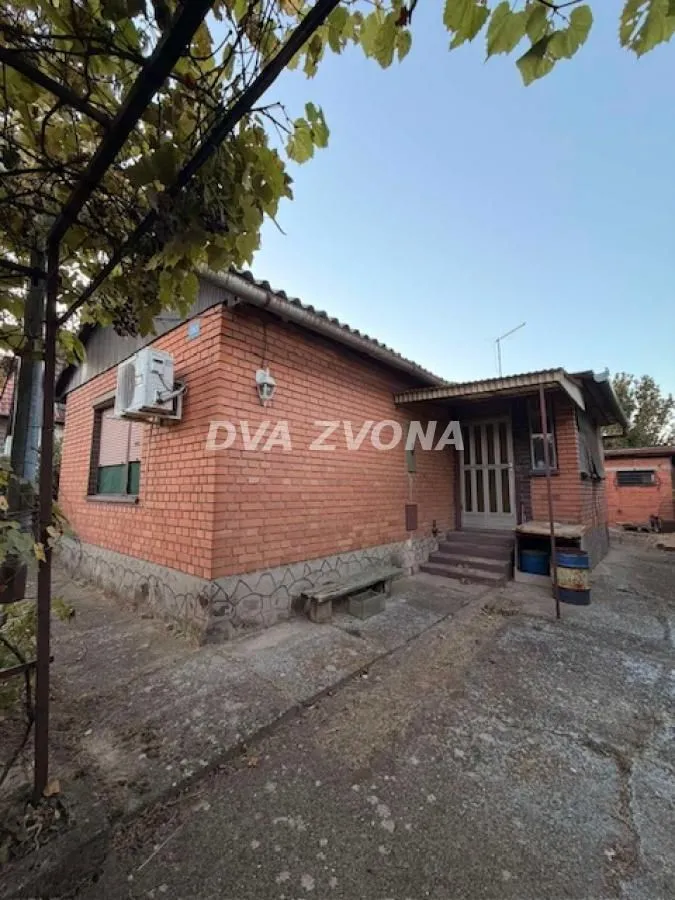 Pogled na spoljašnjost prizemne kuće sa fasadom od cigle i dvorištem.