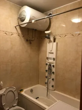Small bathroom with a bathtub, massage shower panel, and a water heater on the wall. - image 8