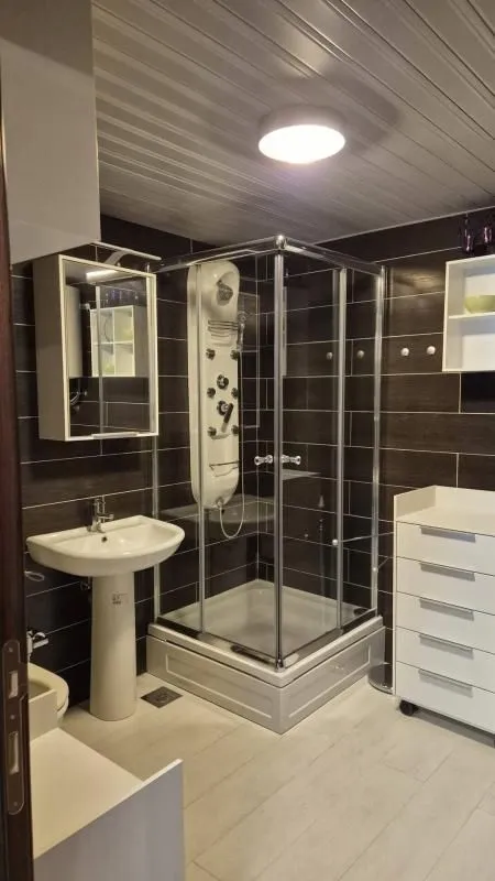 Kupatilo opremljeno tuš kabinom, umivaonikom i bijelim namještajem.