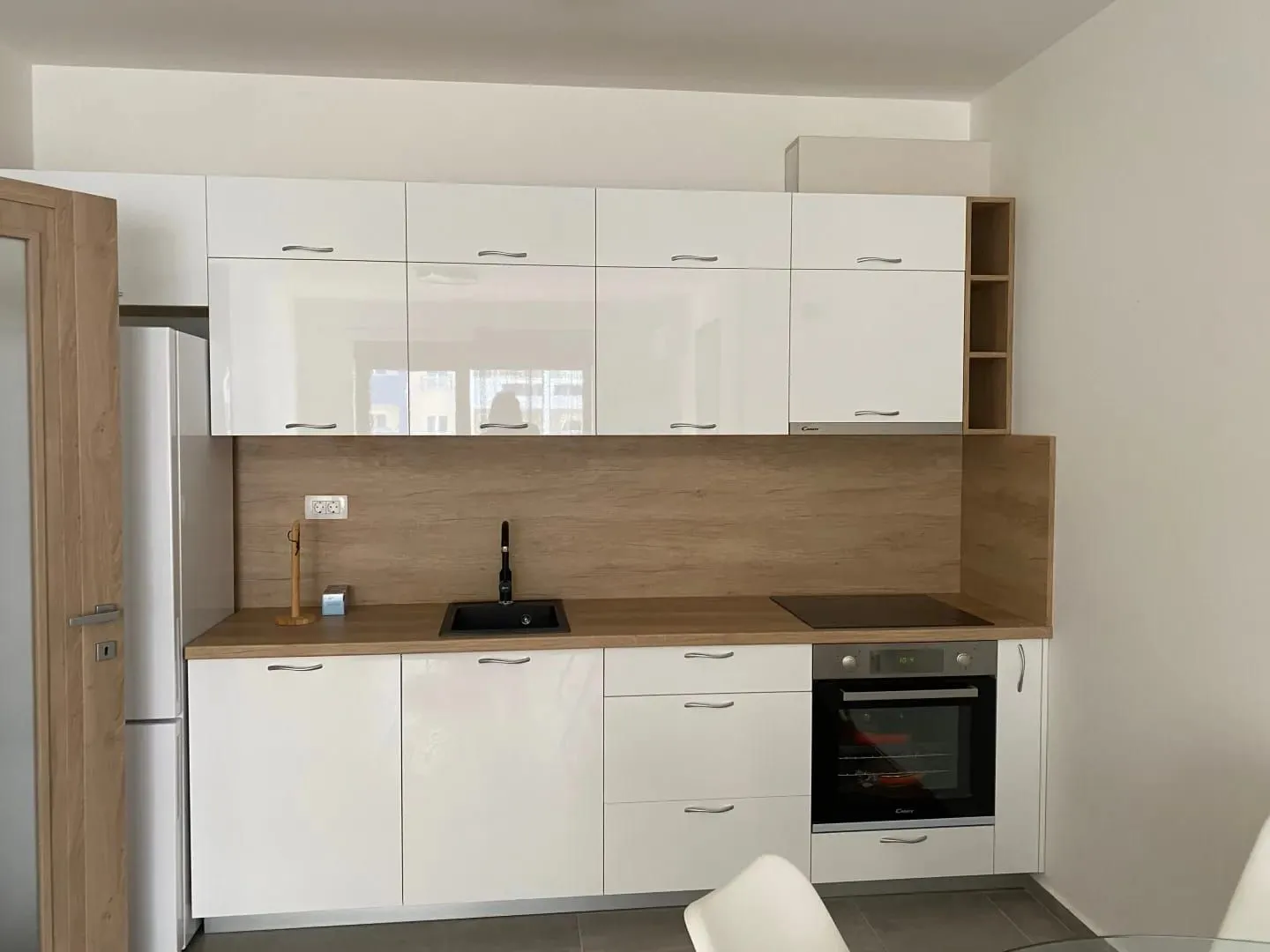 Modern white kitchen with wooden elements and built-in appliances.