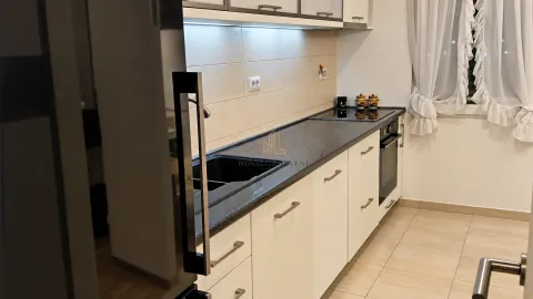 Pogled na moderno opremljenu kuhinju sa bijelim elementima i tamnom radnom površinom. - image 4
